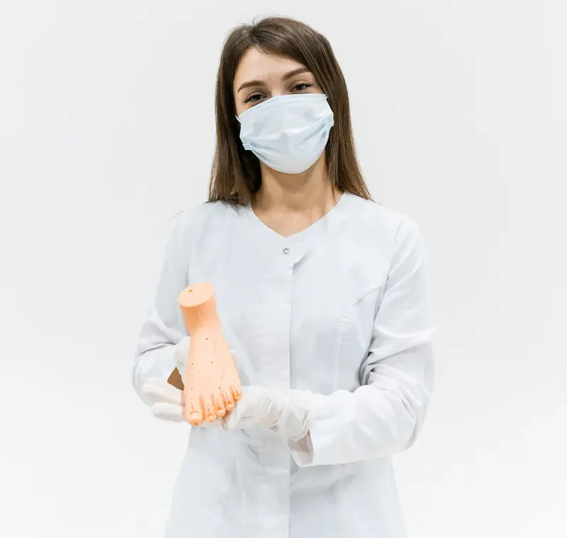 Lekarka w maseczce trzyma model anatomiczny stopy