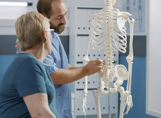 Ortopeda pokazuje starszej pacjentce kręgosłup na modelu szkieletu
